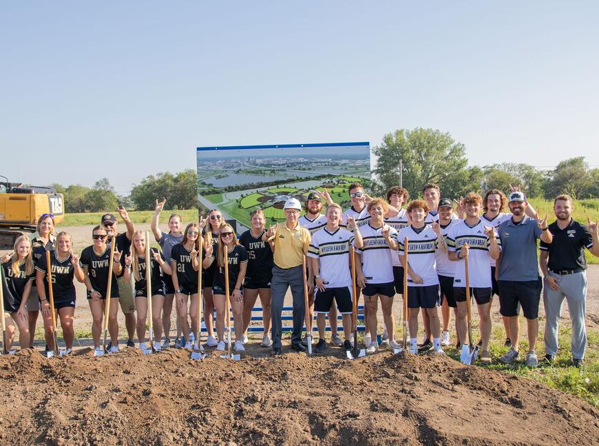 NWU baseball and softball players and coaches surround President Good at sports complex ground breaking.